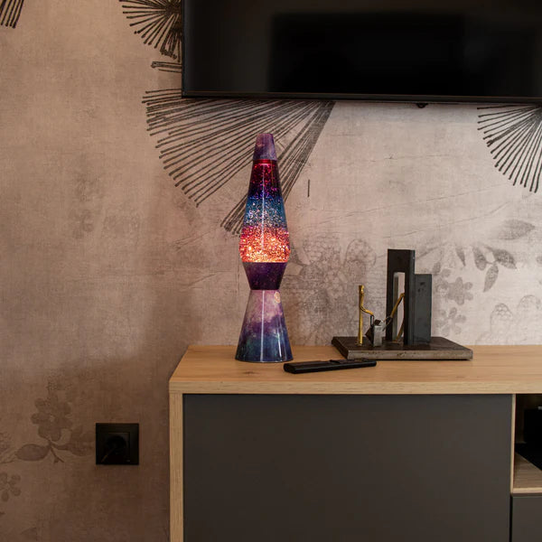 Een afbeelding van de Fisura Kogelvormige Lavalamp met Paarse Lava & Glitter - Galaxy op een kast onder de televisie.