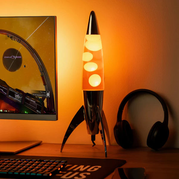 Een foto van de Fisura Raket Lavalamp met Oranje Lava - Chrome, naast een gaming PC.