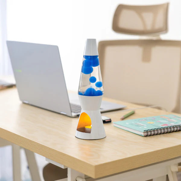 Een foto van de Fisura Theelicht Lavalamp met Blauwe Lava - Wit op een bureau, naast een laptop en wat schrijfgerief.