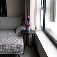 Een foto van de Fisura Kogelvormige Lavalamp met Paarse Lava & Glitter - Galaxy op een salontafeltje aan de raam. 