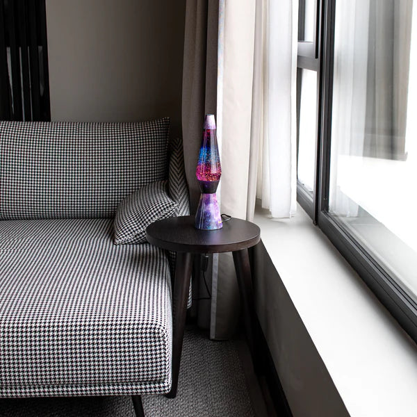 Een foto van de Fisura Kogelvormige Lavalamp met Paarse Lava & Glitter - Galaxy op een salontafeltje aan de raam. 