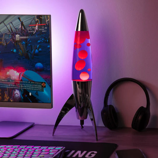 Een foto van de Fisura Raket Lavalamp met Rode & Paarse Lava - Chrome naast een gaming pc.