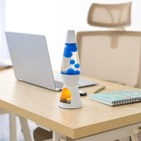Een foto van de Fisura Theelicht Lavalamp met Blauwe Lava - Wit op een bureau, naast een laptop en wat schrijfgerief. 